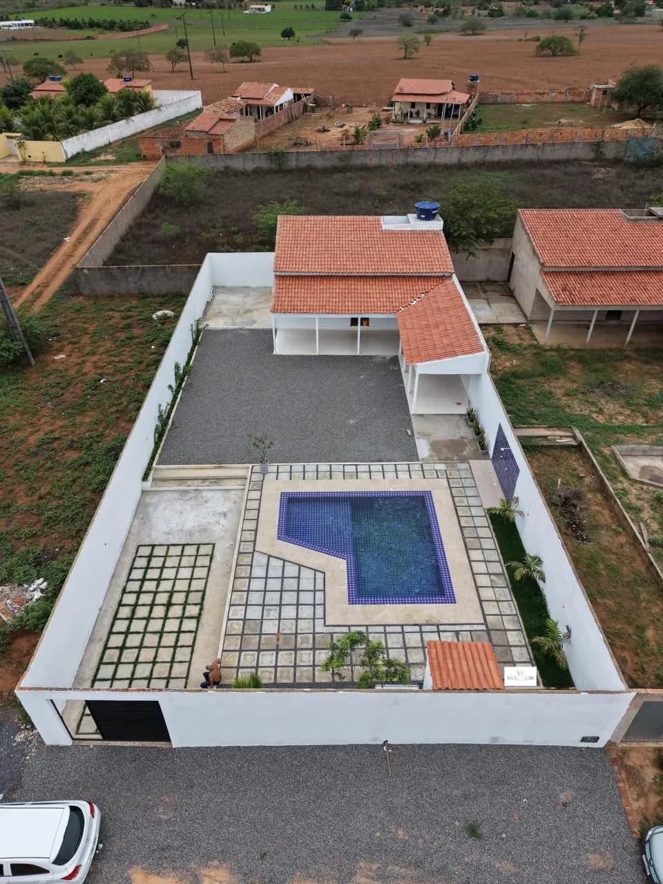 Vista aérea do terreno murado com a casa, a garagem coberta e a piscina